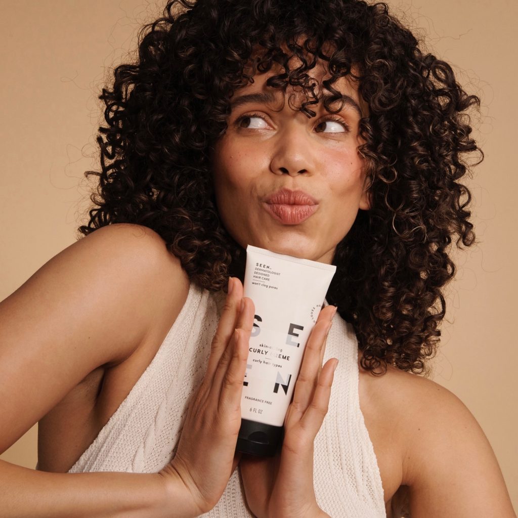 curly haired woman holds SEEN curly creme