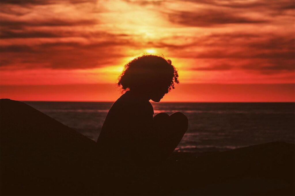 Girl with curly hair silhouetted against a beach sunset